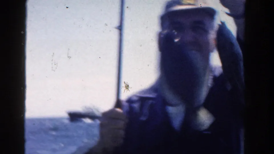 The fisherman holds a large fish close to the camera in 1958 Ontario lake footage, with rod and water visible behind him.