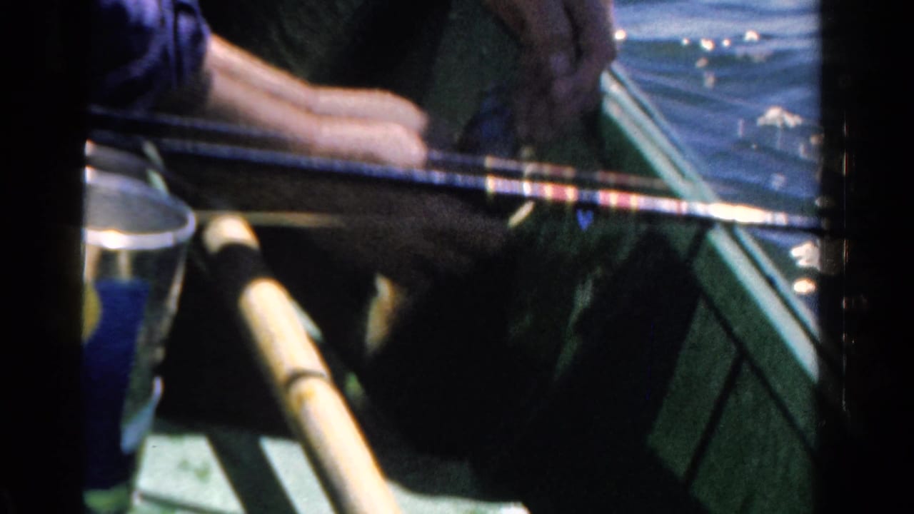 Man's hands in a green boat holding a fishing rod near calm water.