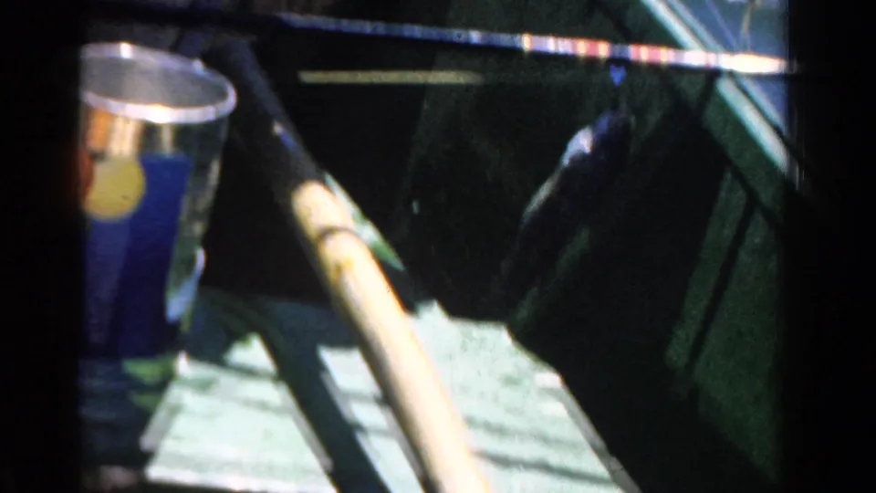 1958 Ontario 8mm frame with a caught fish hanging near the green boat side beneath a fishing rod, with a metal can nearby.