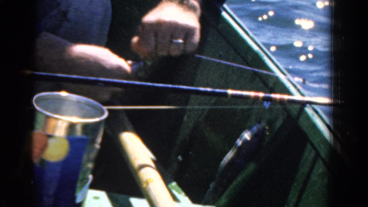 Hands near a fishing rod and bait can in a small boat on water.