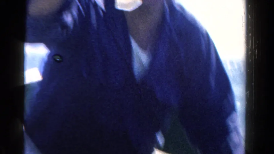 Cropped 1958 Ontario home-movie frame of an adult in a dark shirt leaning inside a small boat in bright light.