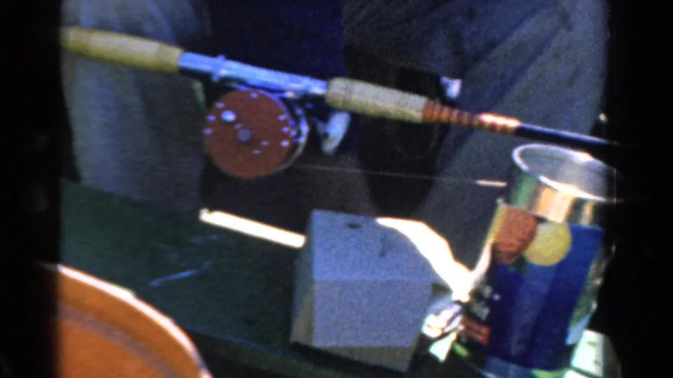 1958 Ontario 8mm frame with a fishing reel and rod above a bait can, with the adult fisher mostly cropped from view.