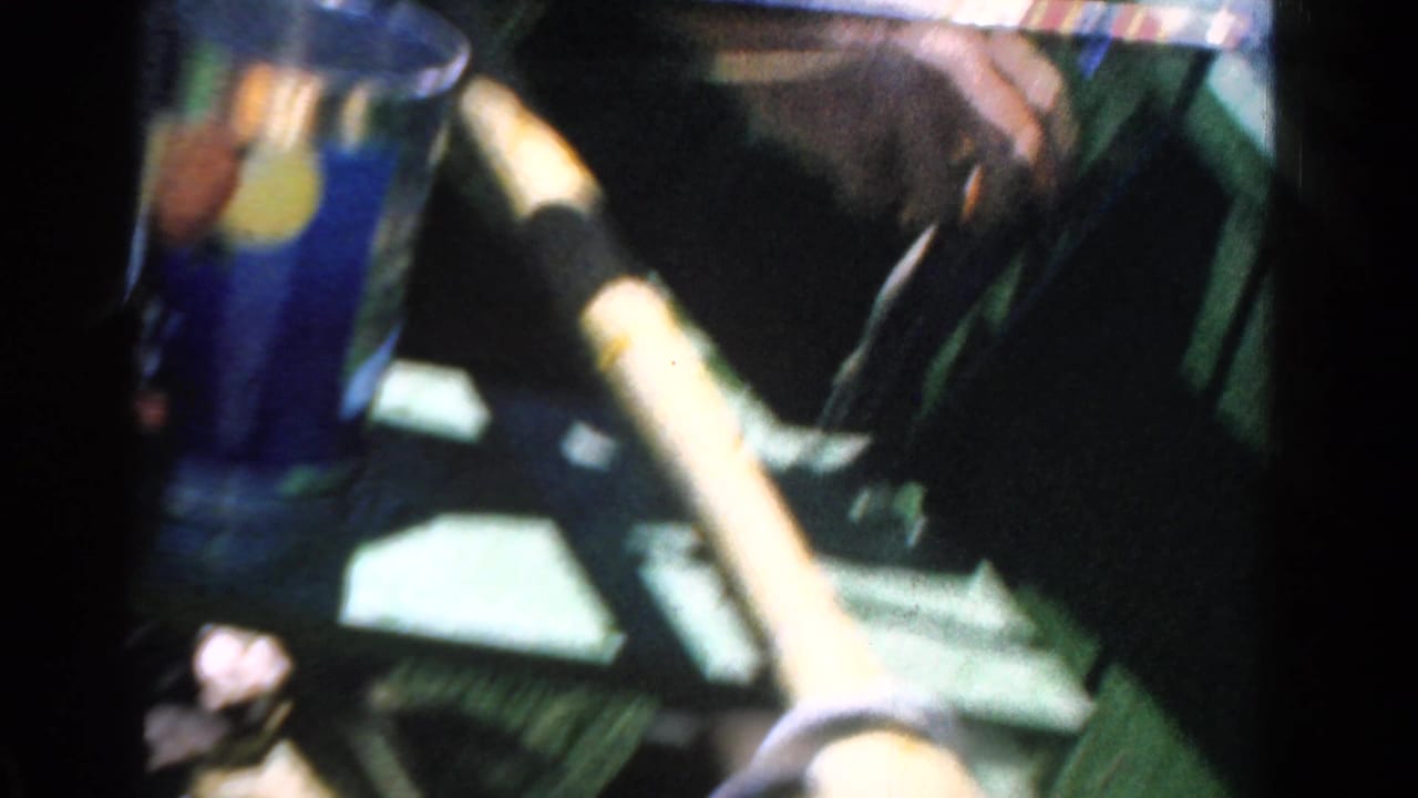 In 1958 Ontario home-movie footage, hands grip a fishing rod inside a small boat beside bright blue lake water.
