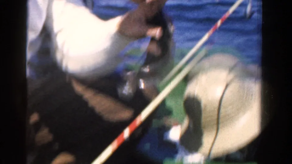 The clip ends on a close 8mm view as the man lowers the caught fish near the rod and hat inside the boat on Ontario water.