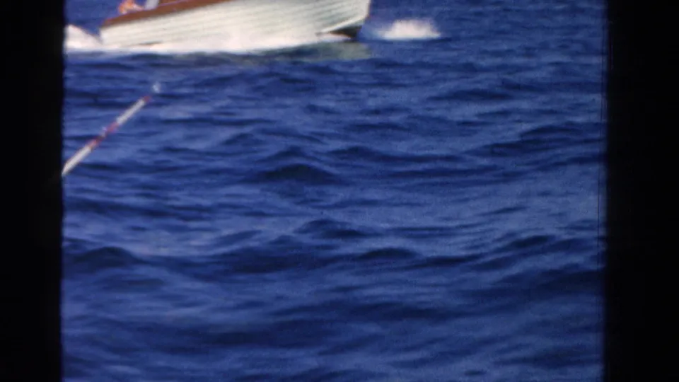A fishing rod extends from the filming boat as a white motorboat passes across the blue water in a 1958 Ontario home-movie frame.