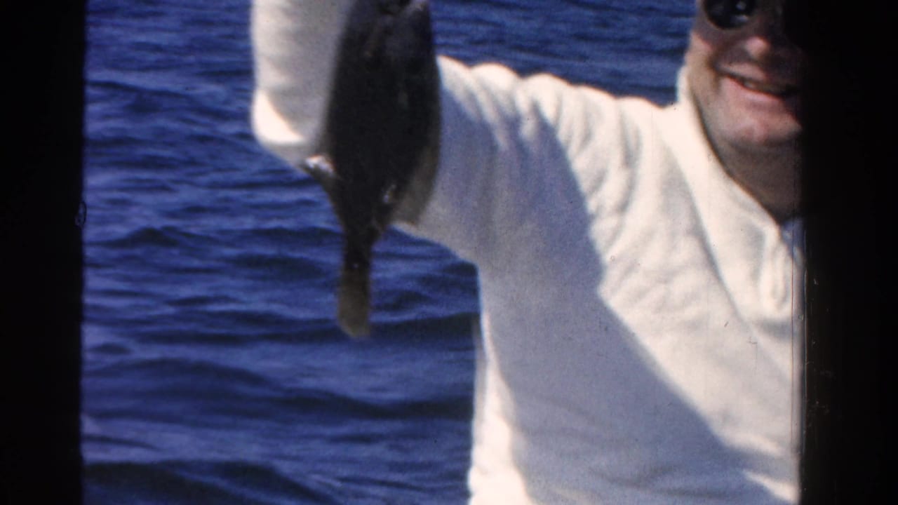 Smiling man in sunglasses holds up a fish against blue open water.