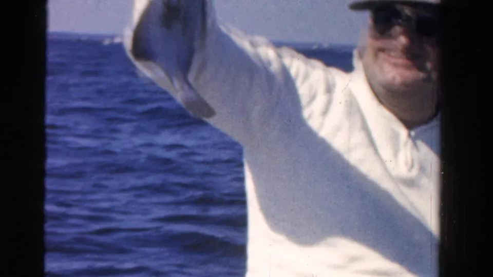 The fisherman remains on the boat, partly cropped, with bright blue open water behind him.