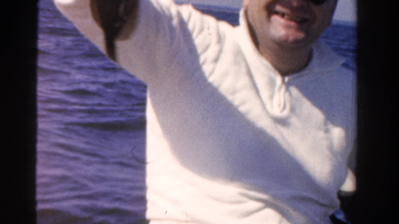 Smiling man in a white sweater stands near blue water with dark 8mm frame borders.