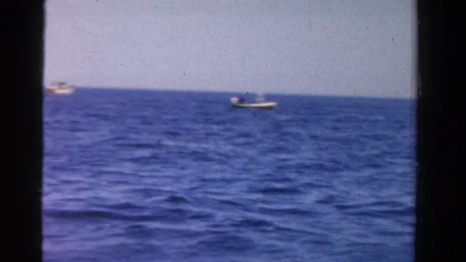 A wide 1958 Ontario home-movie view shows open water, clear sky and a small boat in the distance near the horizon.