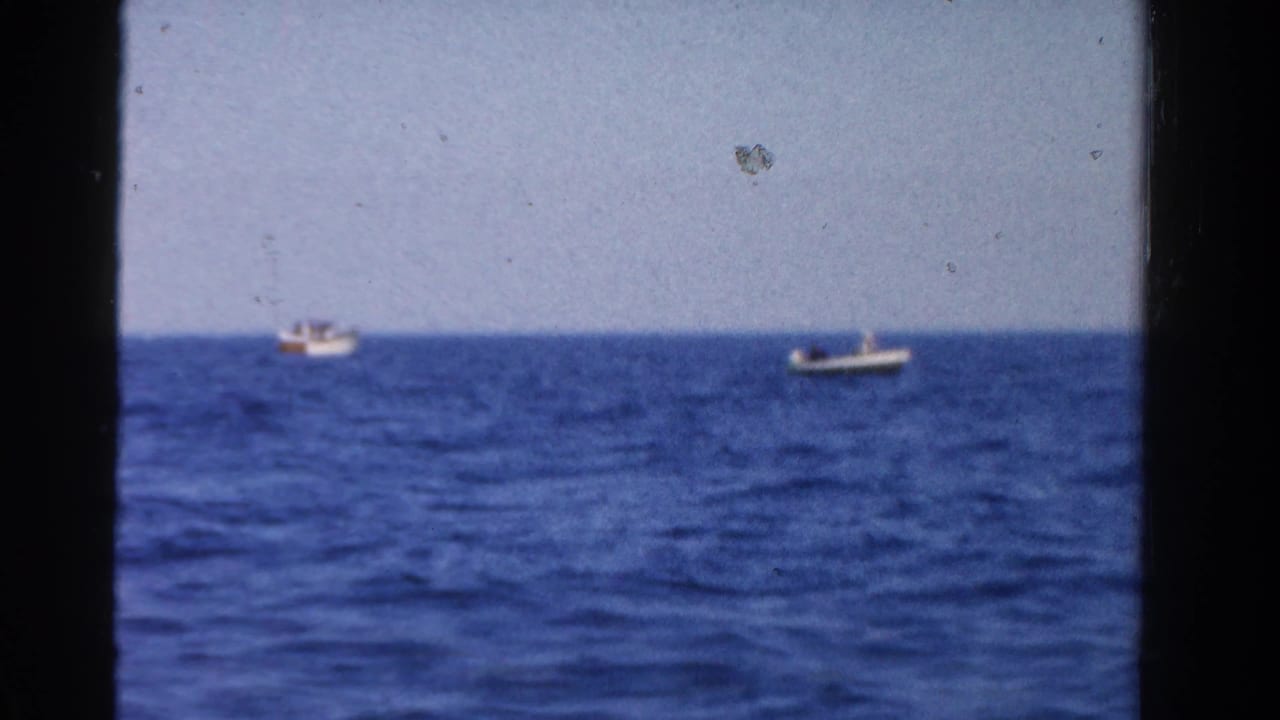 Two small boats sit far apart on blue open water beneath a pale sky.