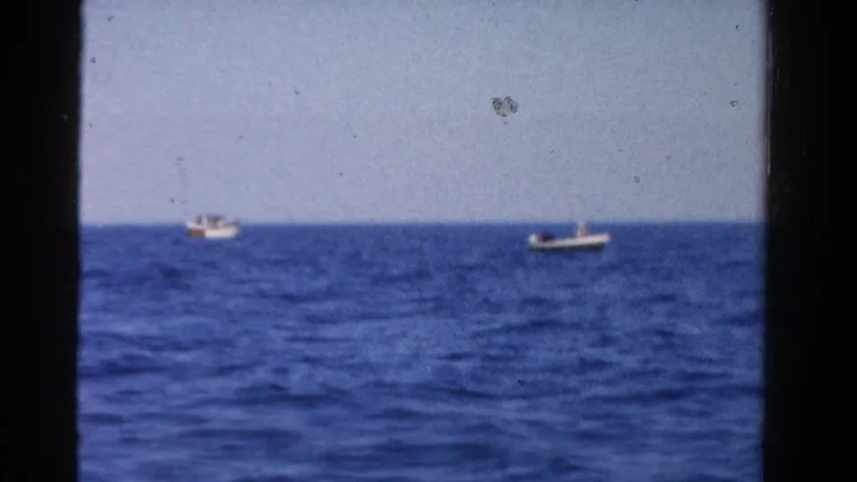 1958 Ontario home-movie frame showing two small distant boats on open blue water with a level horizon and soft 8mm color.