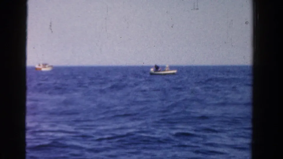 1958 Ontario 8mm frame with small boats near the horizon, rippled water in the foreground, and dark film edges visible.