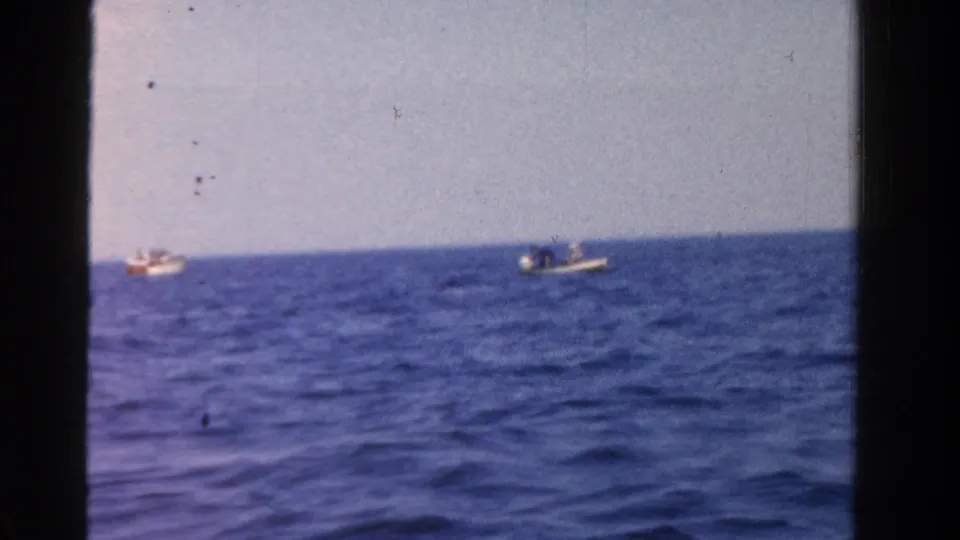1958 Ontario home-movie view of two distant small boats on blue water, framed by visible 8mm film borders and a pale sky.