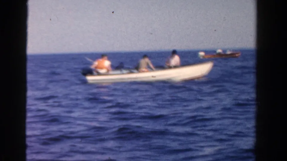 1958 Ontario 8mm frame showing an open motorboat with three seated people, one in an orange life vest, on rippled blue water.