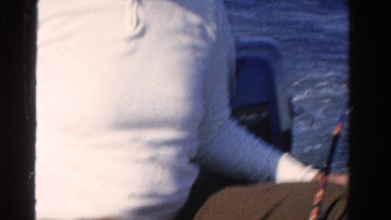 1958 Ontario home-movie frame showing a cropped adult man in a white shirt on a boat, with blue water in the background.