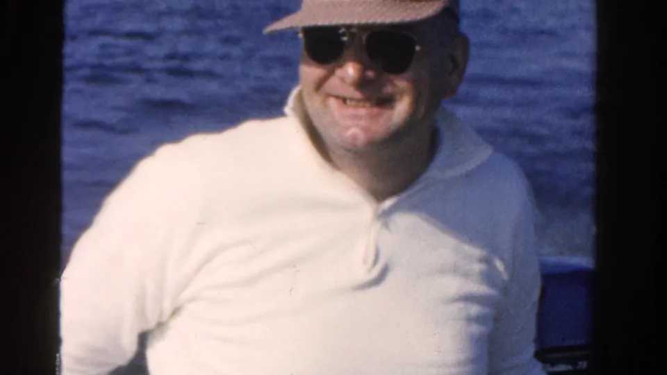 A smiling adult man in a straw hat, sunglasses, and white shirt appears on a boat in Ontario in 1958.