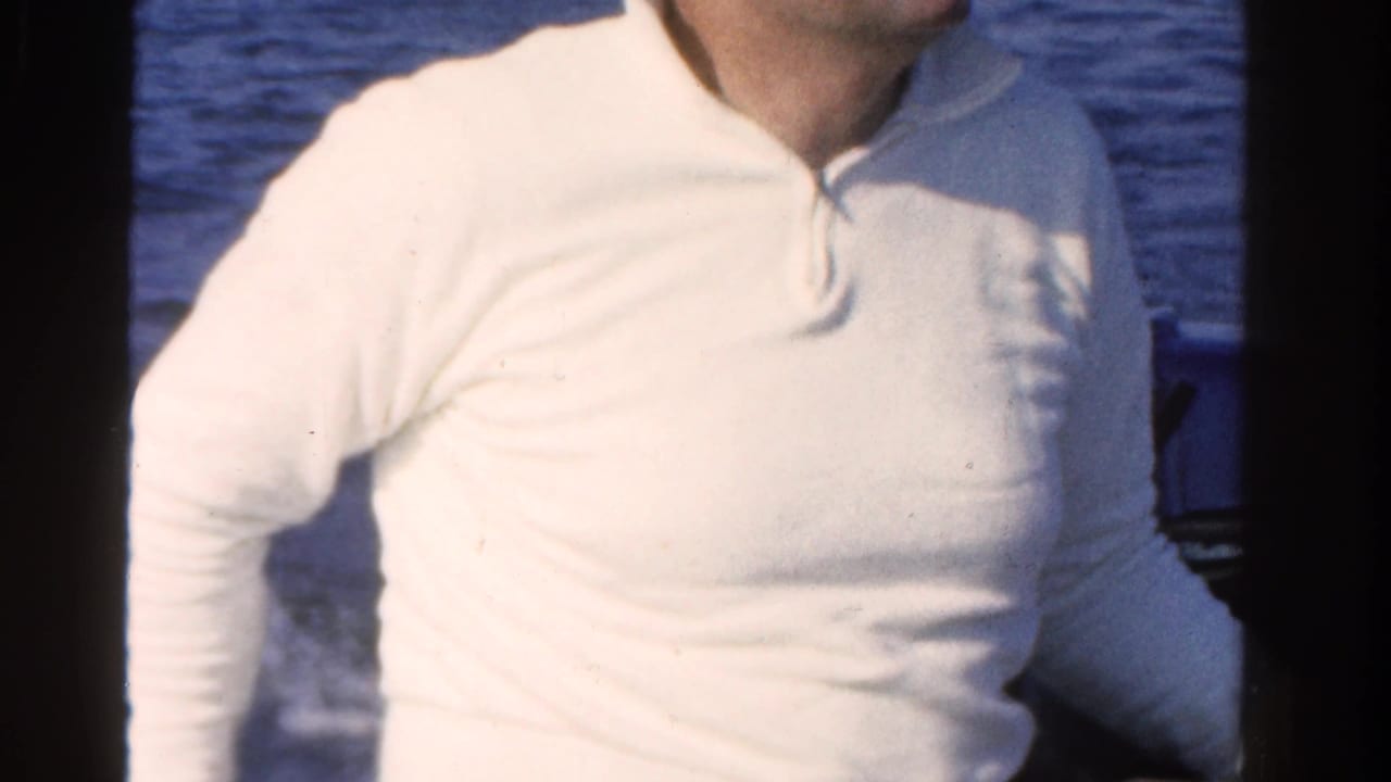 A man in a white shirt stands close to the camera during a 1958 Ontario boating scene, with blue water visible behind him.