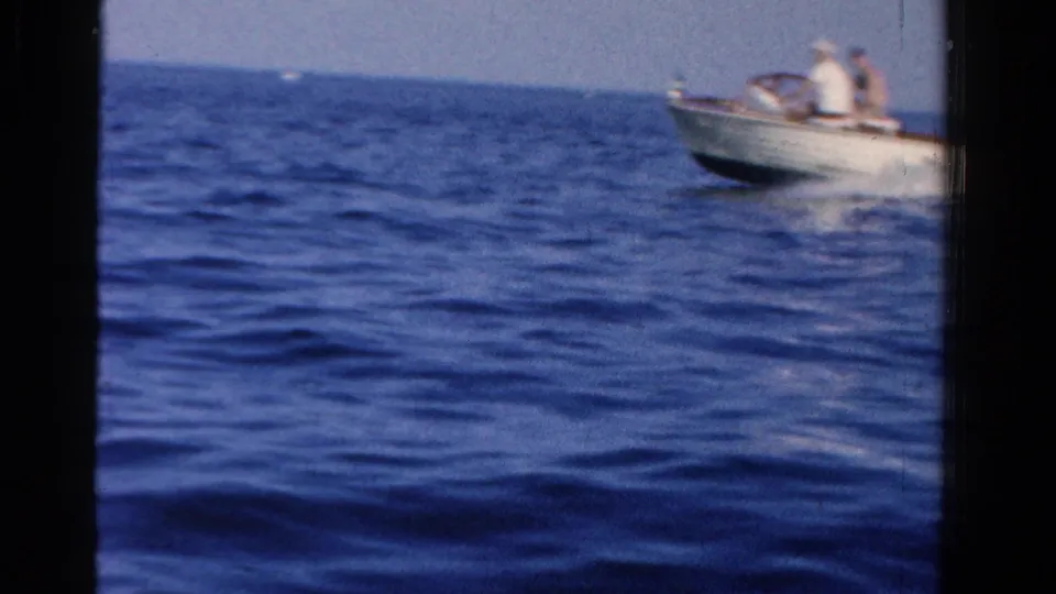 A small motorboat with passengers appears on blue water in the 1958 Ontario home-movie boating footage.