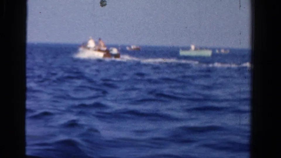 A distant motorboat with passengers leaves a wake across open water in the 1958 Ontario home-movie scene.