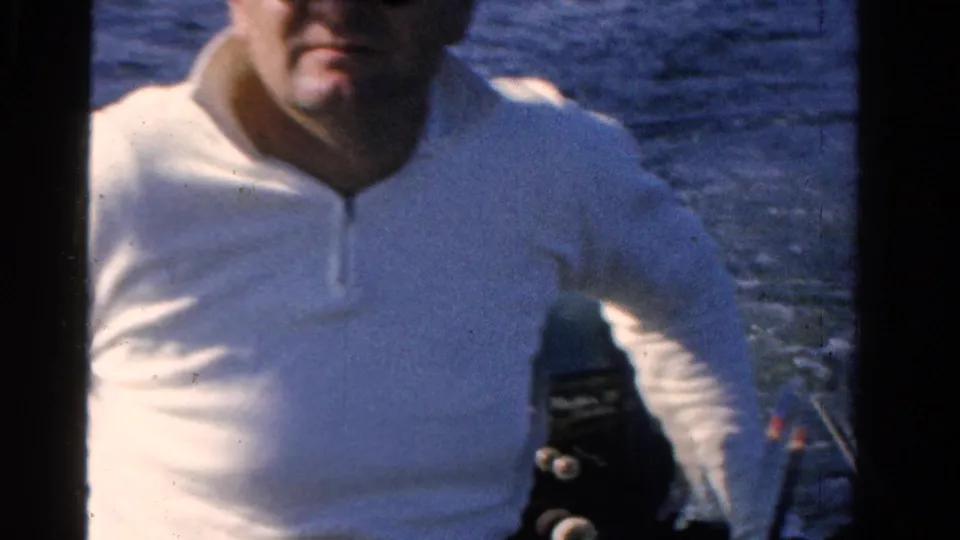 Adult man wearing sunglasses and a white shirt stands by boat equipment on a blue Ontario lake in 1958 8mm footage.