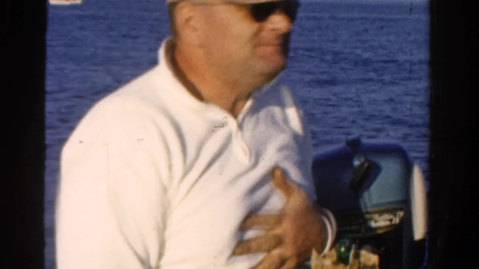 The man sits near an outboard motor after drinking, with open Ontario water behind him in the 1958 8mm home-movie clip.