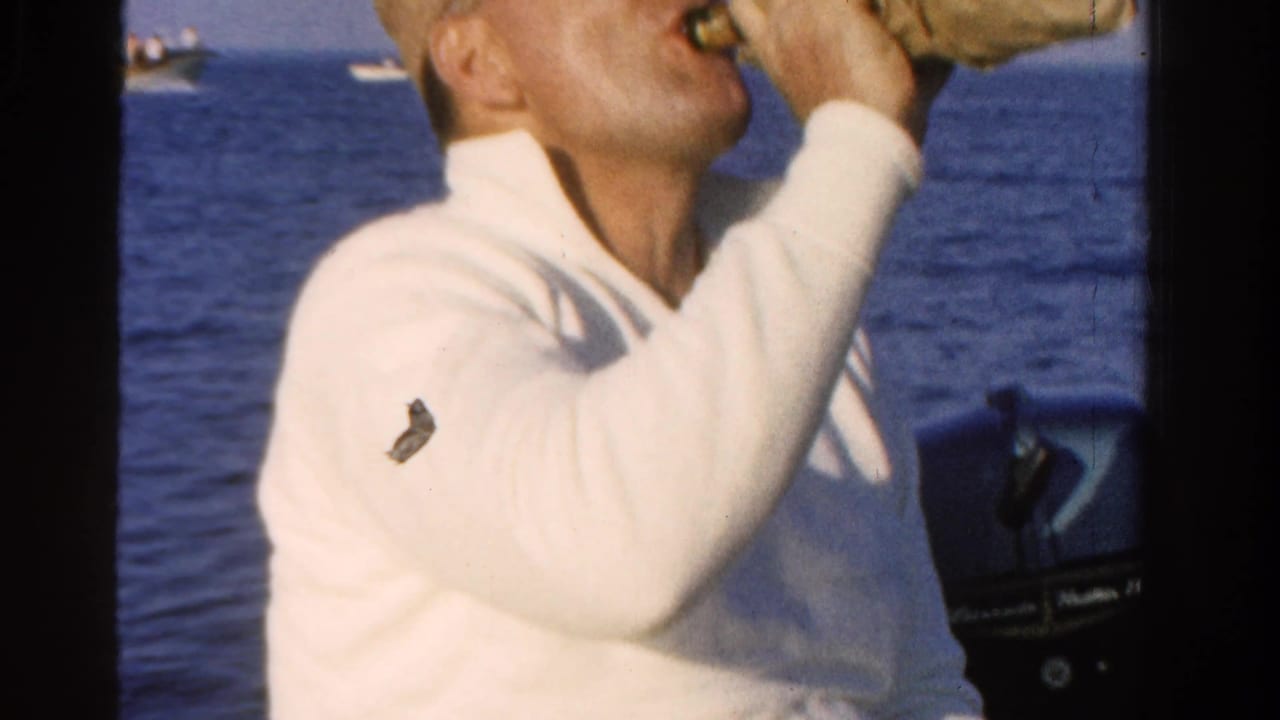 Man in a white shirt and straw hat drinks from a bottle on a boat.