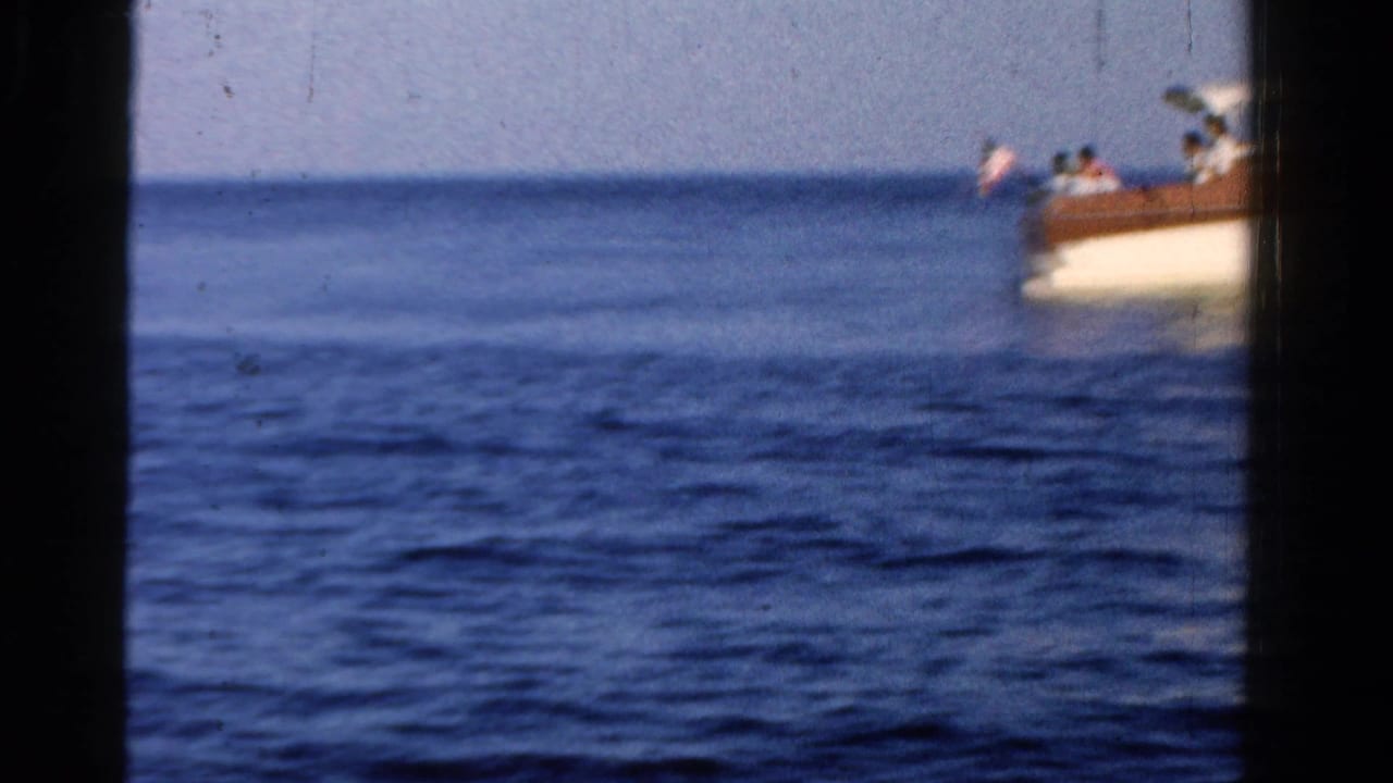Classic motorboat moving across calm blue water with passengers visible near the cabin.