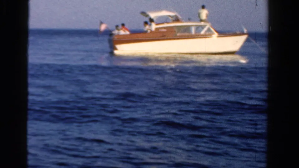 The motorboat continues across the water, with passengers seated near the cabin and one person standing at the rear.
