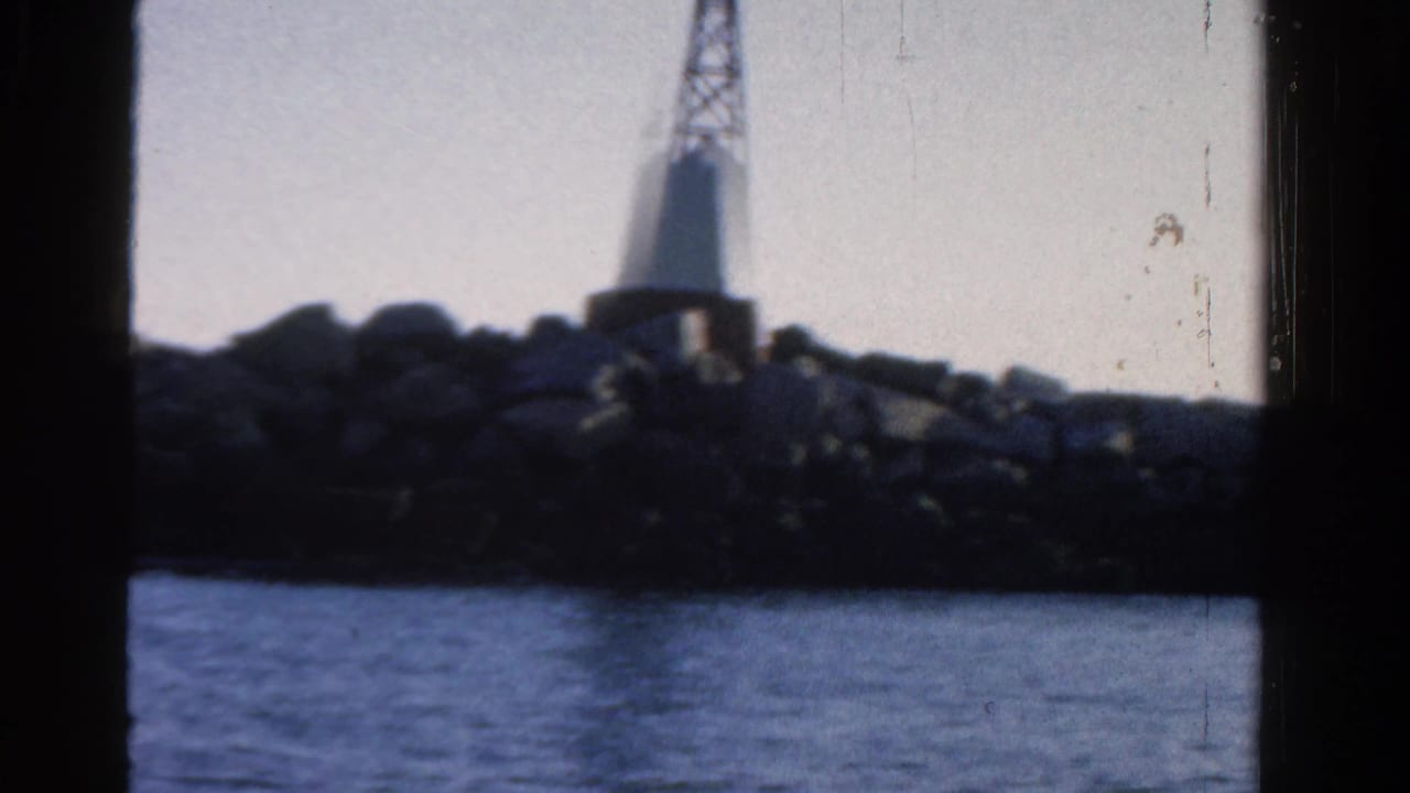 White lighthouse on a rocky jetty across calm blue water.