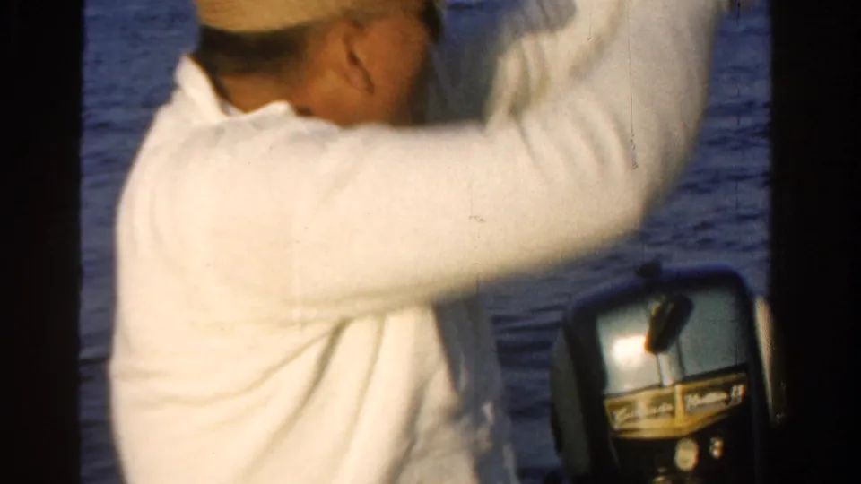 An adult man in a white long-sleeved shirt is partly visible near an outboard motor, with water and rocks behind him.