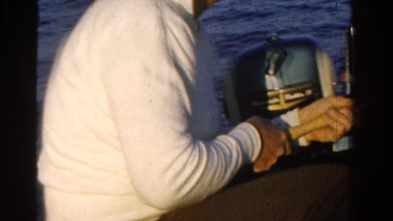 Man in a white shirt sits beside an outboard motor on open water.