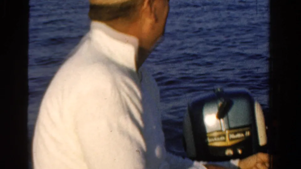 The man turns toward the water in the small motorboat, with the outboard motor and open water visible behind him.