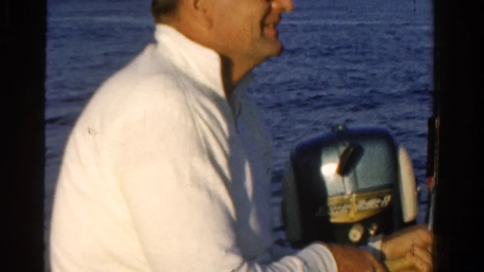 A smiling man in a white shirt sits close to the outboard motor during a 1958 Ontario fishing outing on open water.