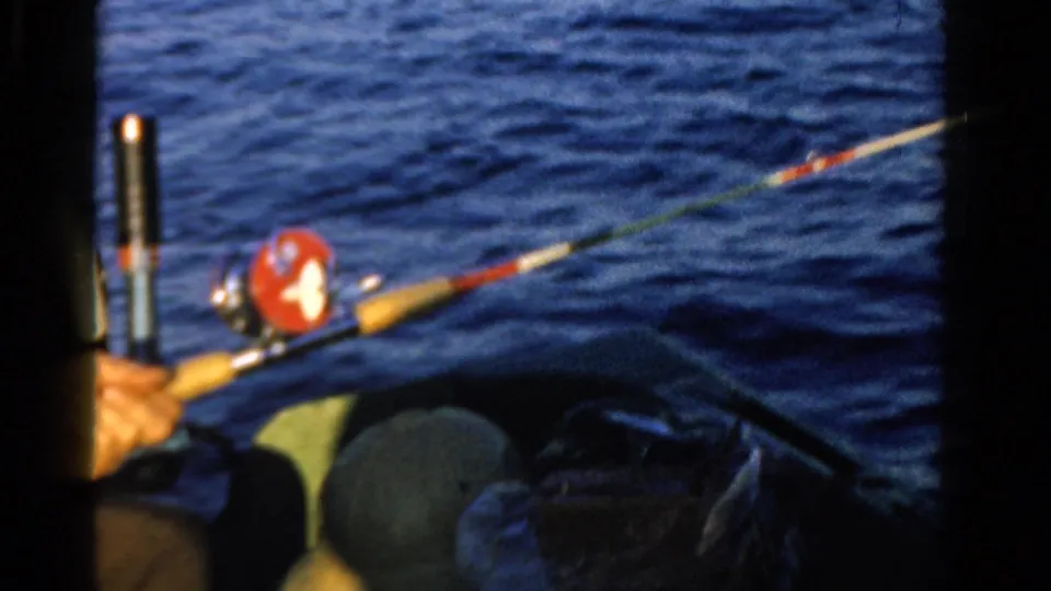 A fishing rod with a red reel extends from the boat over rippled Ontario water in the 1958 home-movie clip.