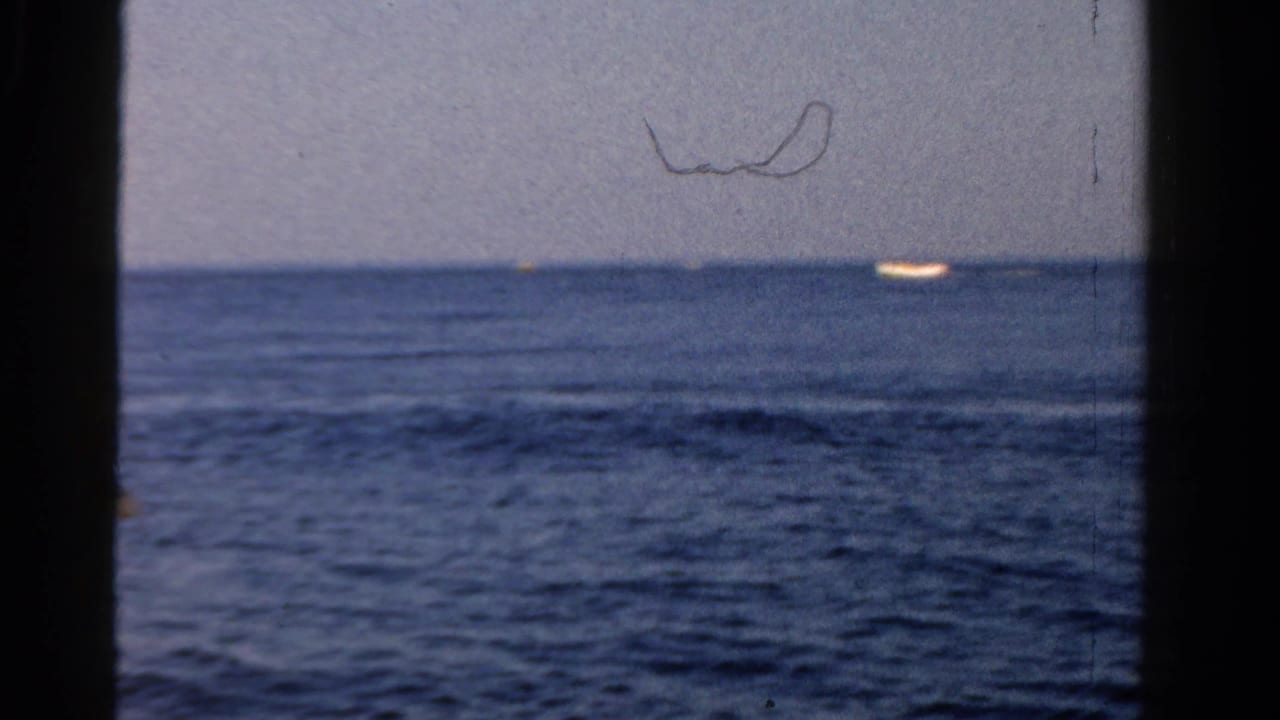 Open blue water under a pale sky with a small bright boat near the horizon and dark frame edges.
