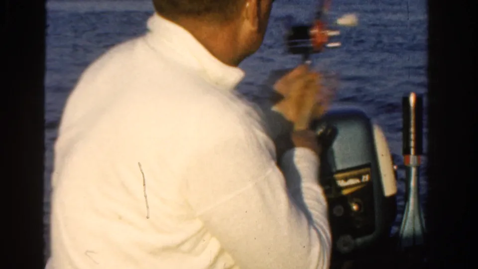Adult man in a white sweater sits near an outboard motor on a 1958 Ontario boat, with fishing tackle and open water behind him.