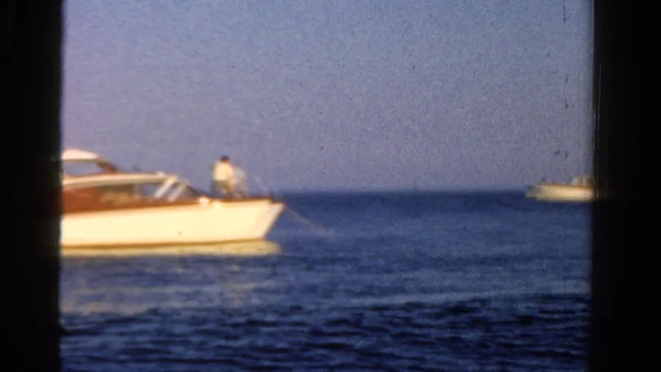 1958 Ontario 8mm frame showing a white motorboat with wood trim on calm blue water, with distant boats and dark frame edges.