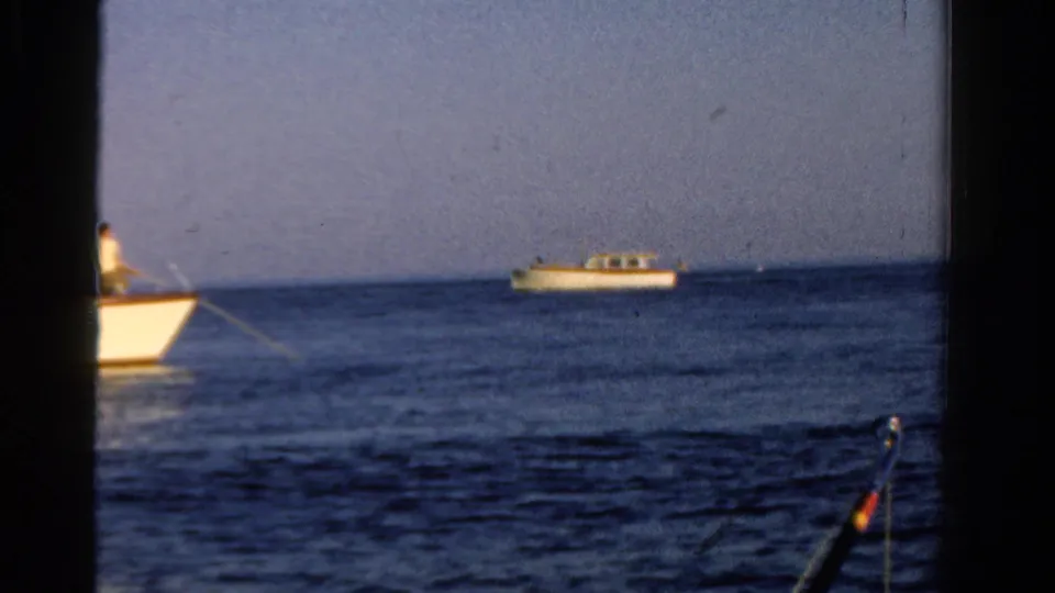 1958 Ontario home-movie frame of motorboats on calm water, divided by a dark window or film-frame edge.
