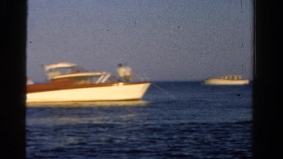 1958 Ontario 8mm still showing a classic motorboat with a standing man aboard and another boat beyond it.