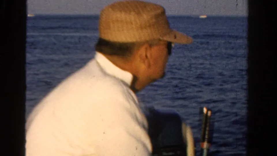 In 1958 Ontario home-movie footage, a man in a straw hat sits on a boat and looks across calm water.