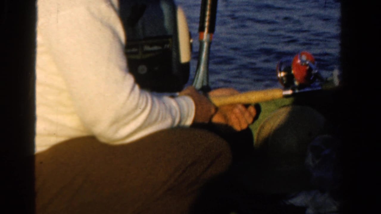 Close view of a seated person holding a fishing rod beside boat equipment and water.