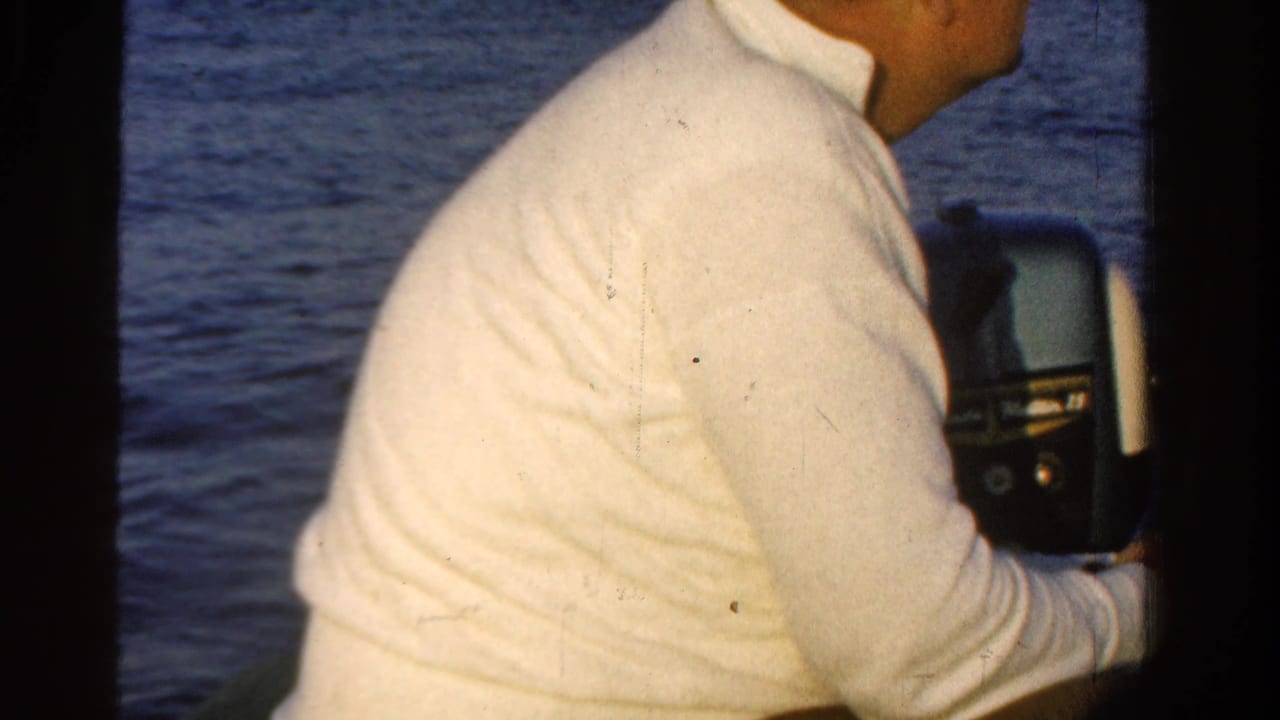Man in a white long-sleeved shirt seated inside a boat looking toward open water.