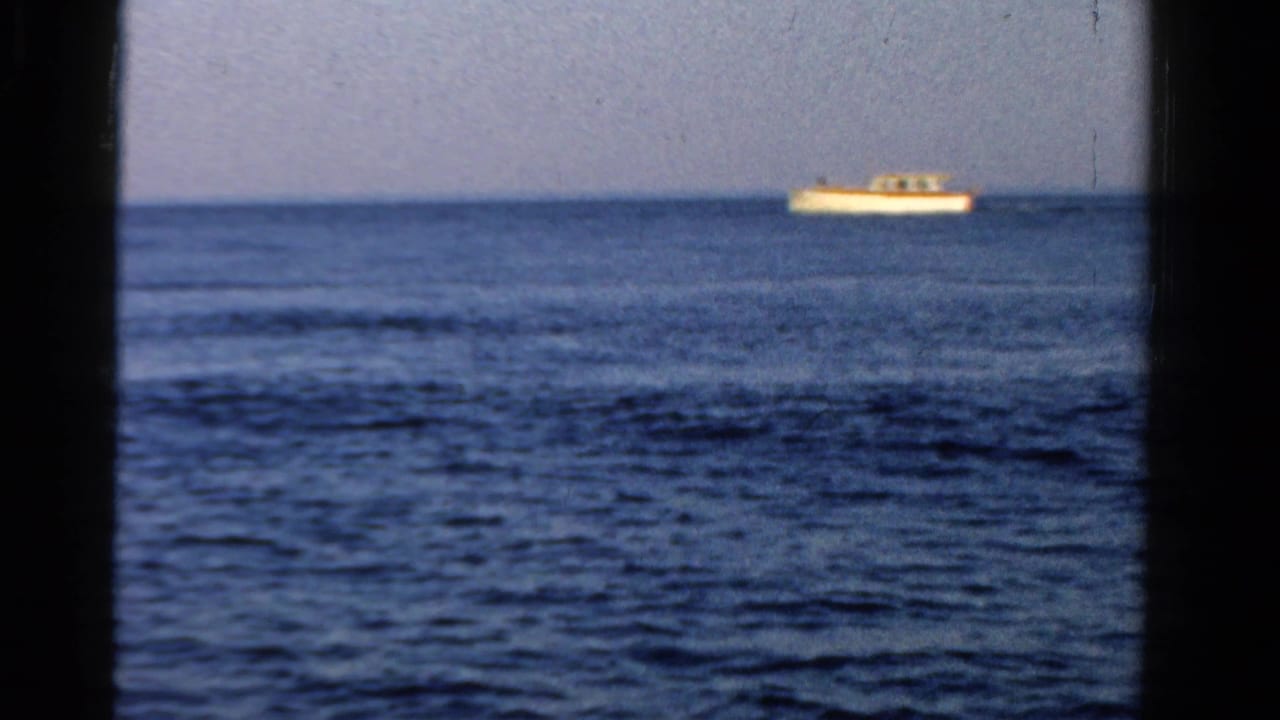 Small white boat floating near the horizon on blue open water.