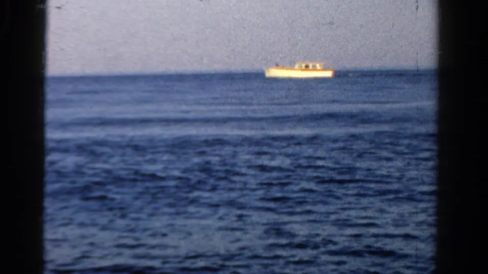 A distant white boat crosses the upper frame over rippled blue water in this 1958 Ontario 8mm home-movie still.