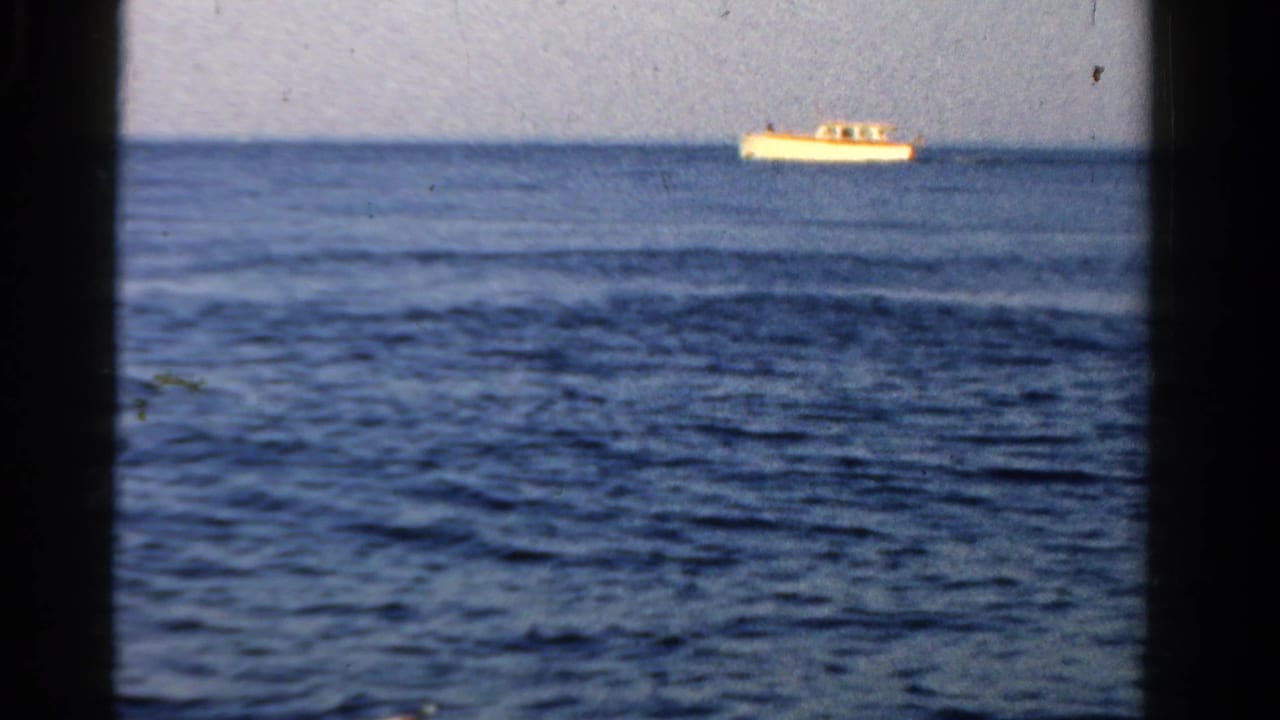 1958 Ontario home-movie view of a distant motorboat on open water, framed by dark vertical edges and visible film grain.