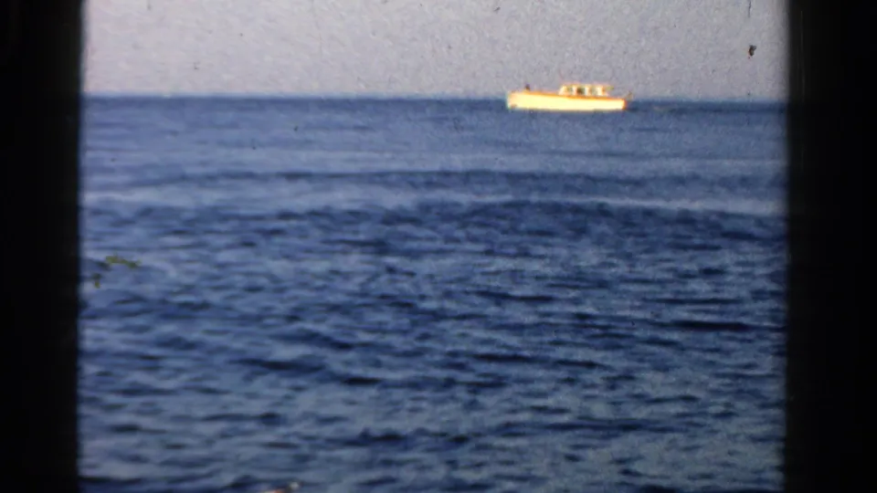 1958 Ontario home-movie view of a distant motorboat on open water, framed by dark vertical edges and visible film grain.