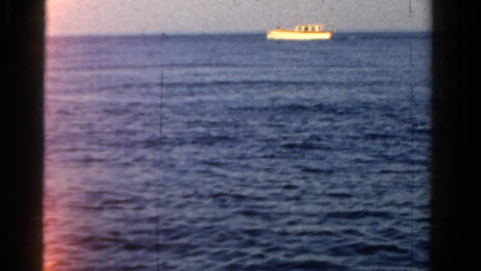 8mm frame from the 1958 Ontario boating clip with a small motorboat on calm water and visible color shift along the film edge.