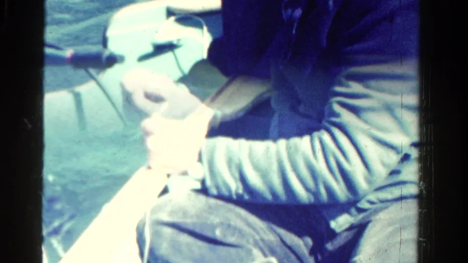 Brief 1958 Ontario home-movie frame showing a seated passenger in blue clothing on a boat, partially cropped and overexposed by sunlight.