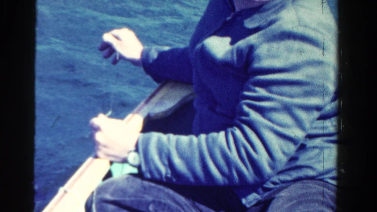 Close view of a seated man holding an oar above calm blue water.