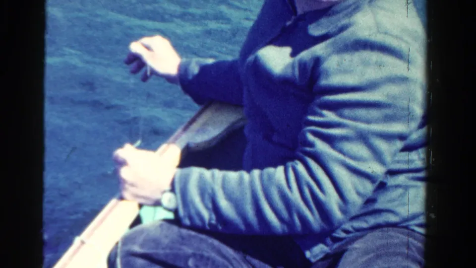 A man in a blue jacket holds an oar in a small boat, with calm Ontario lake water behind him, according to the clip metadata.